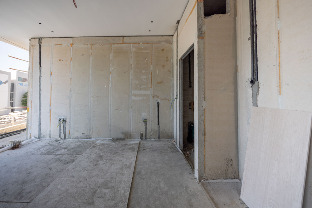 Cove Edition I By Imtiaz 1 An unfinished room with bare walls, exposed wiring, and an open doorway, showing a construction setting.